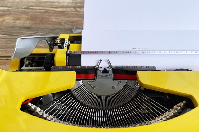 yellow typewriter with paper stating new script 